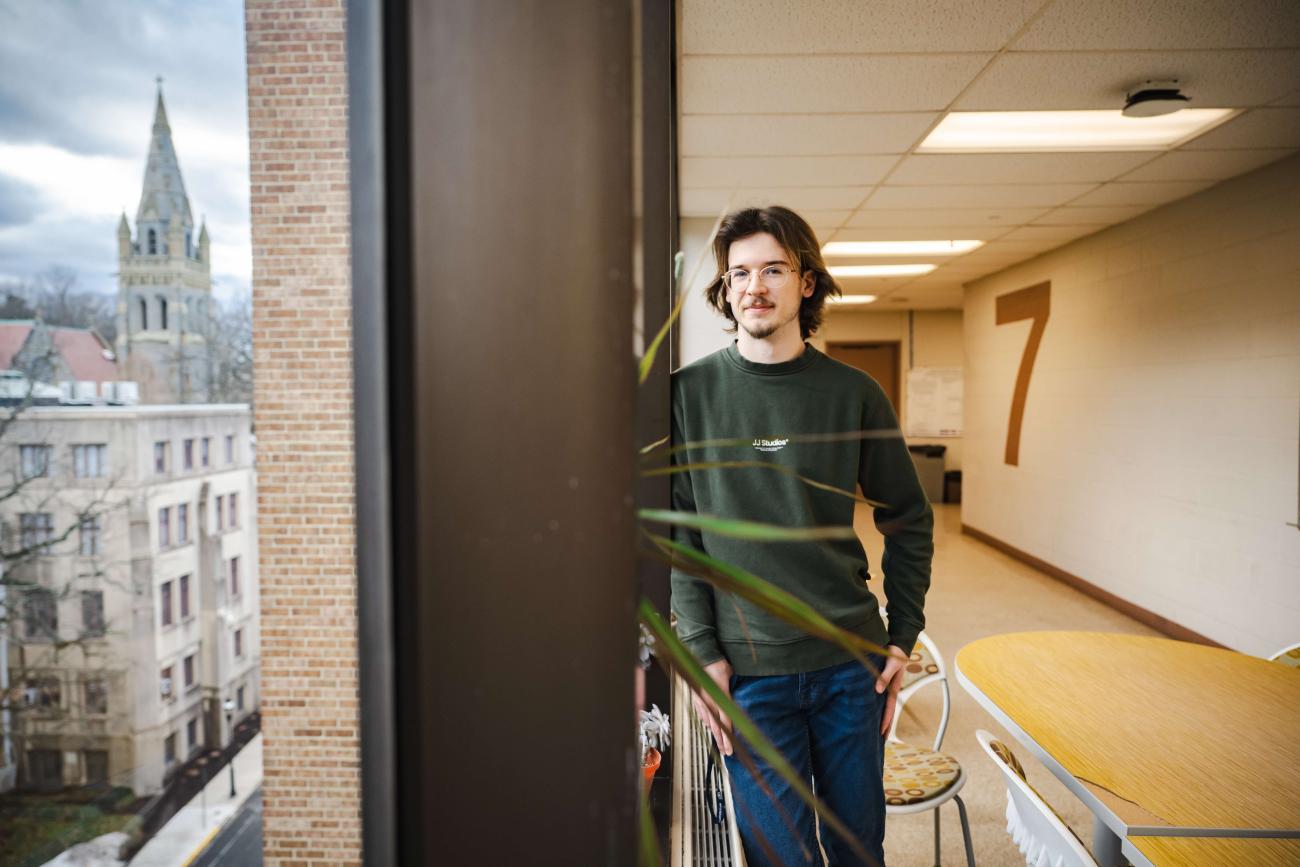 Matthew Reeves stands on the 7th floor of Mudd and leans against a window.